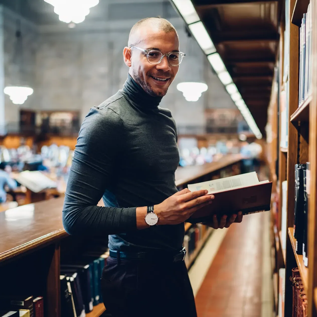 A confident man in a modern law library holding a legal textbook, representing students in the Legal Studies program.